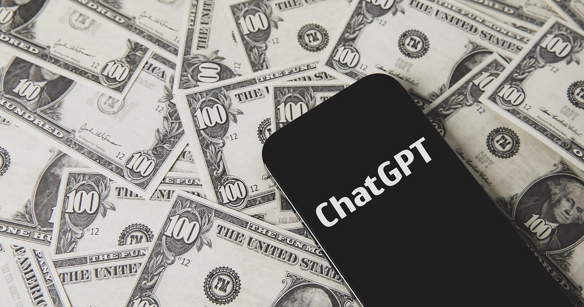 Celular com a palavra ChatGPT na tela sobre notas de 100 dólares espalhadas